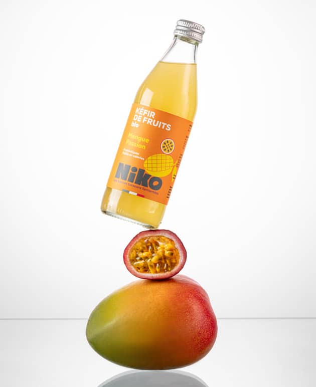 Bouteille de kéfir de fruits mangue passion 33 cl bio Niko en équilibre sur une mangue et un fruit de la passion