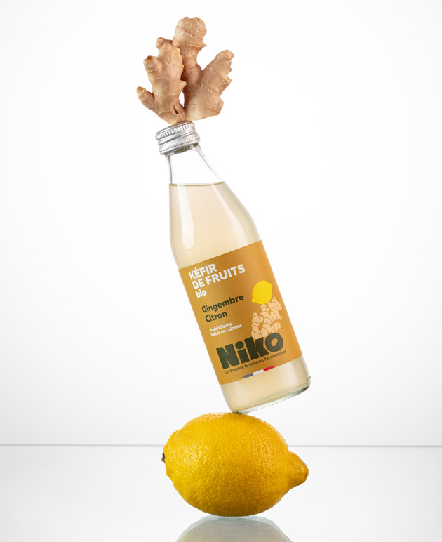Bouteille de kéfir de fruits gingembre citron bio Niko en équilibre sur un citron avec racine de gingembre