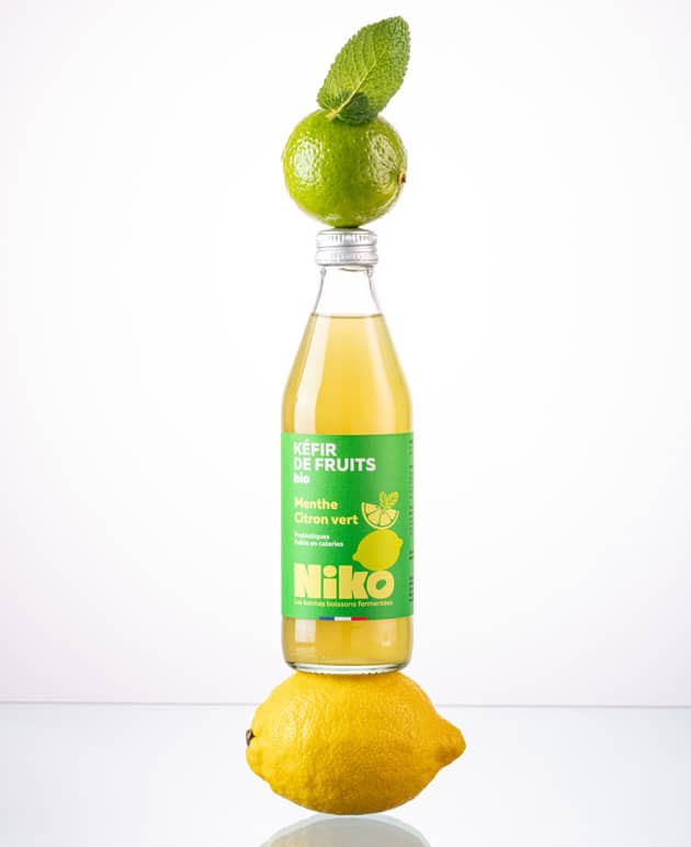 Bouteille de kéfir de fruits menthe citron vert bio Niko en équilibre sur un citron et un citron vert avec feuille de menthe