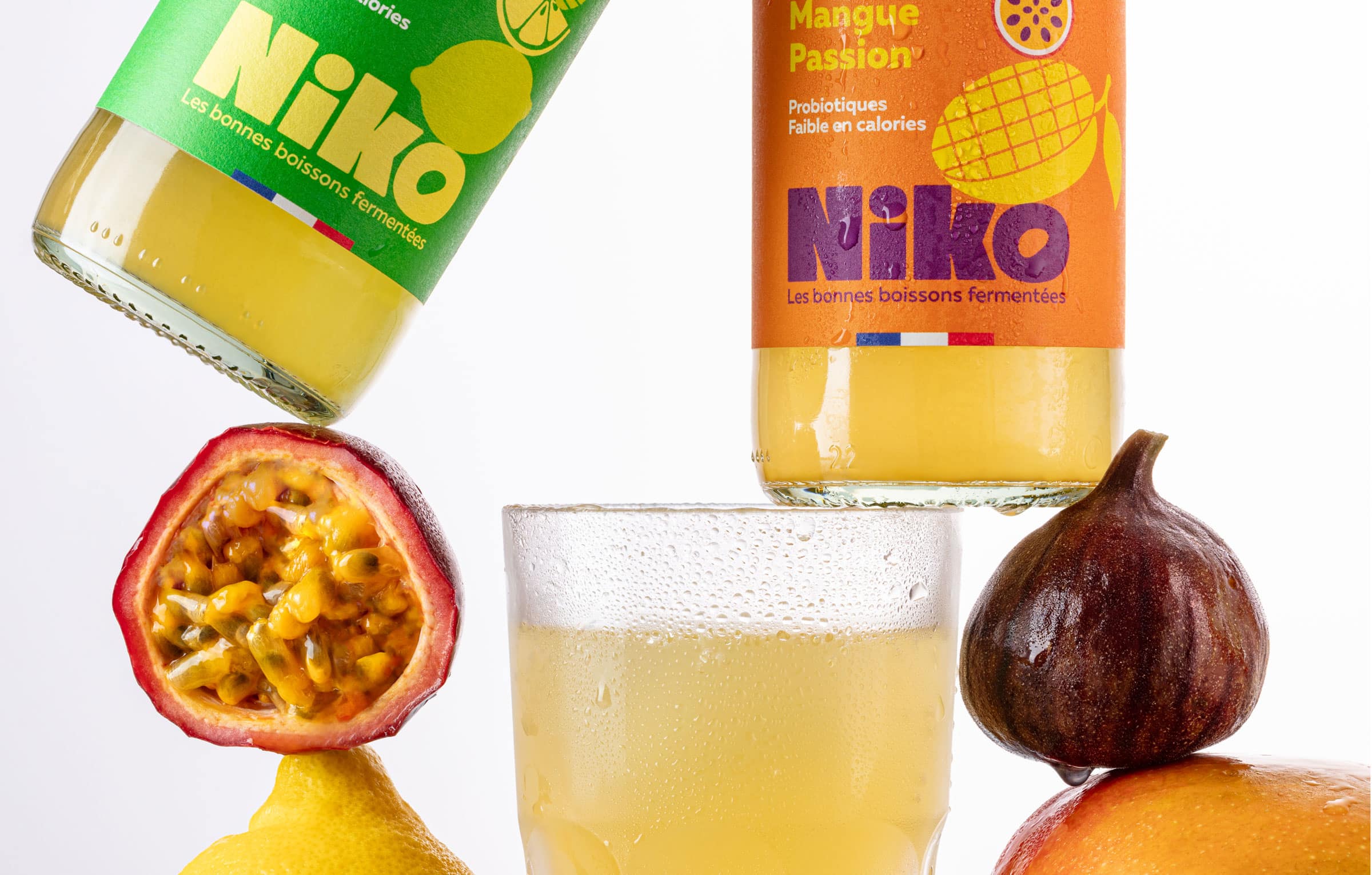 Bouteilles de kéfir de fruits Niko aux saveurs mangue passion et menthe citron vert autour d’un verre avec fruits frais